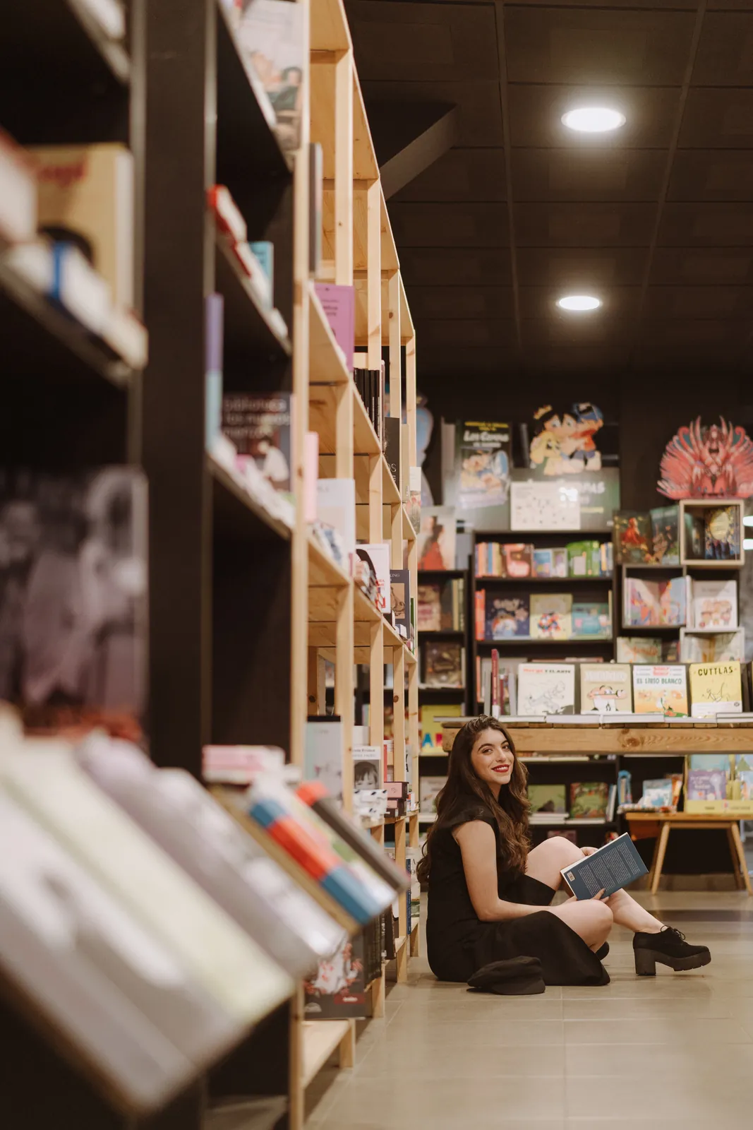 Silvia Nieto sentada en el suelo de una librería leyendo un libro entre estanterías